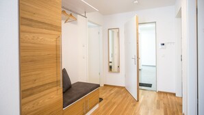 Ein modernes Zimmer mit einem Holzschrank, einer Bank mit Kissen, einem Spiegel und einer Tür zu einem weiteren Raum.