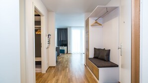 Ein modernes Apartment mit Holzboden, einer Sitzecke mit Kissen, einem Kleiderschrank und einer Küche im Hintergrund.