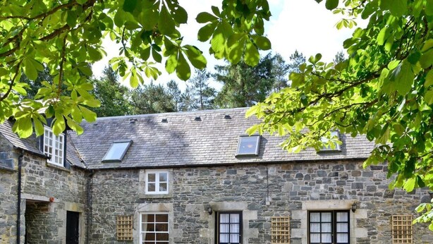 Edificio in pietra con cortile interno, caratterizzato da un ampio spazio aperto con pavimento in pietra, diverse finestre e un tetto spiovente con lucernari.