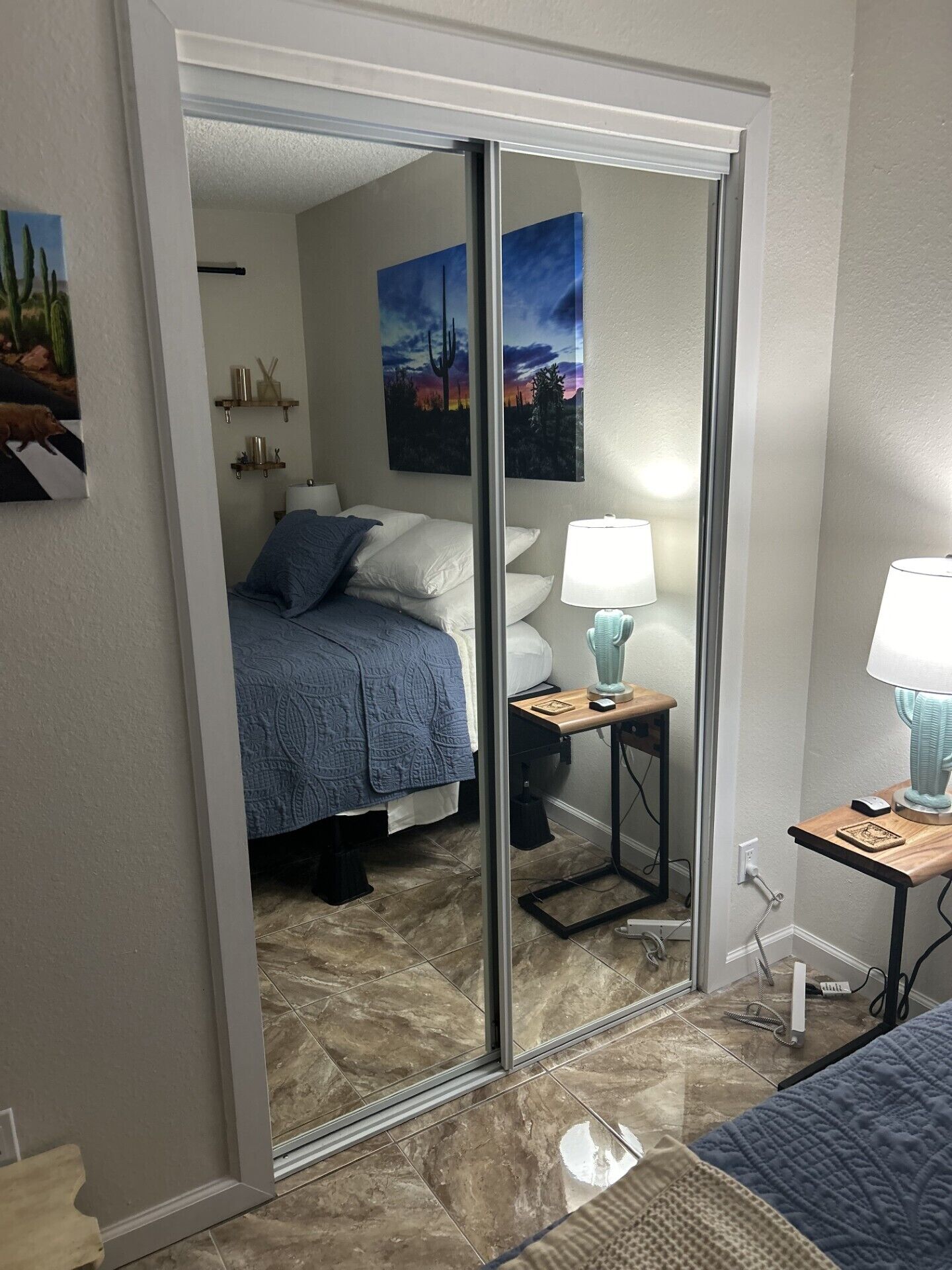 A hotel room with a bed, a nightstand with a lamp, a mirror, and artwork on the walls.