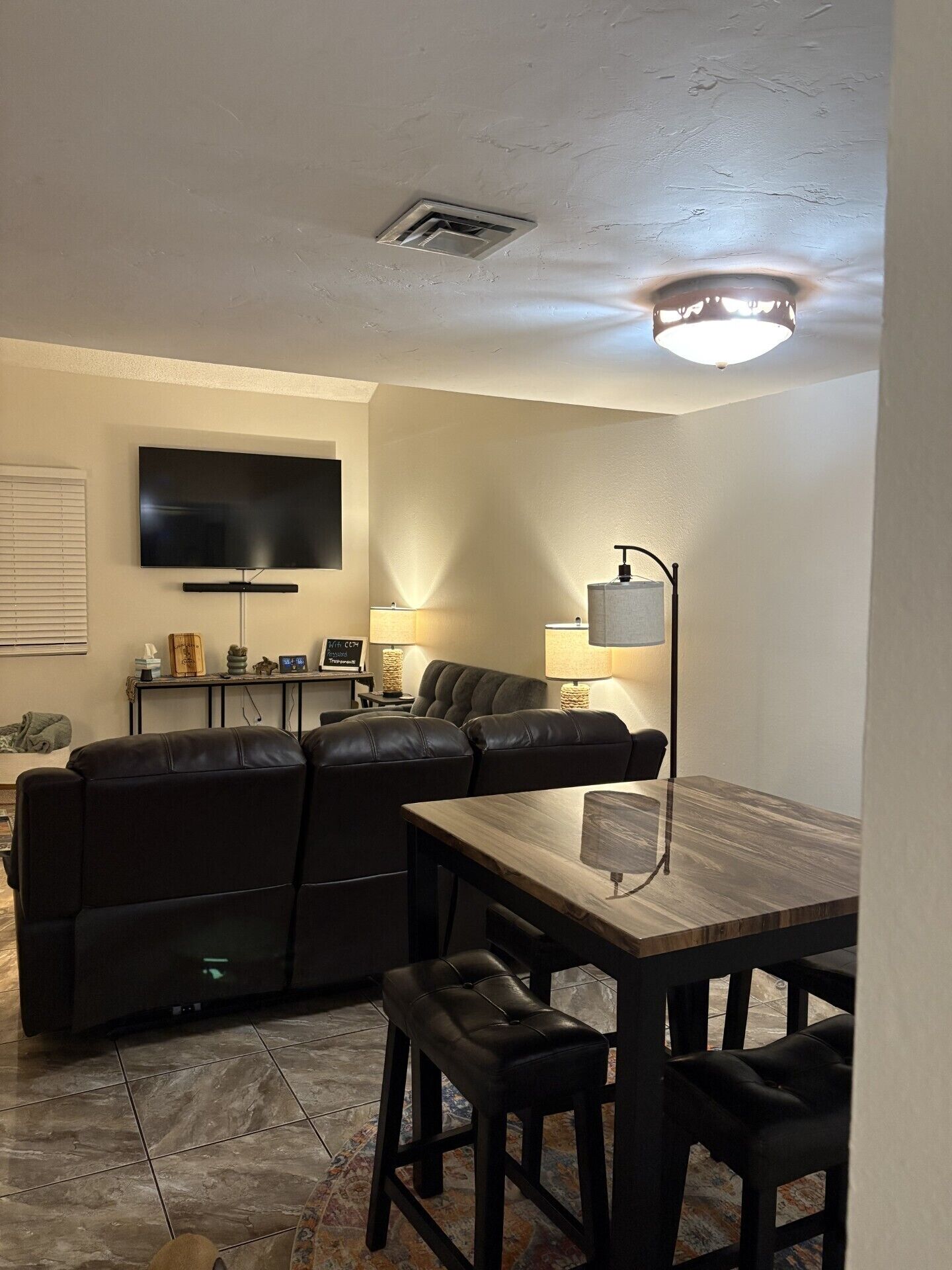 A living room with a flat-screen TV, leather sofa, and a dining table with chairs.