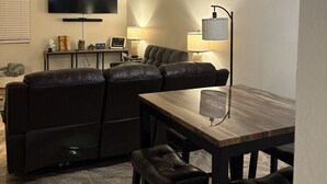En stue med et fladskærms-TV, lædersofa og et spisebord med stole.