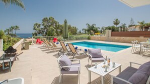 Un espace aménagé au bord de la piscine, avec des chaises longues, une table où sont posées des boissons, et une vue sur l’océan.