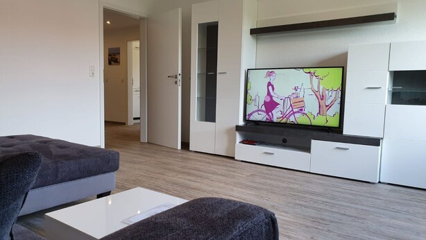Ett modernt vardagsrum med en platt-TV, en grå soffa och ett vitt soffbord.