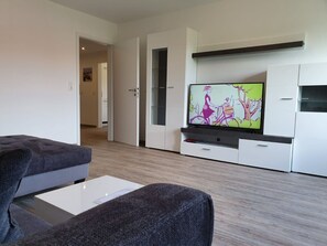 Un salon moderne avec un téléviseur à écran plat, un canapé gris et une table basse blanche.