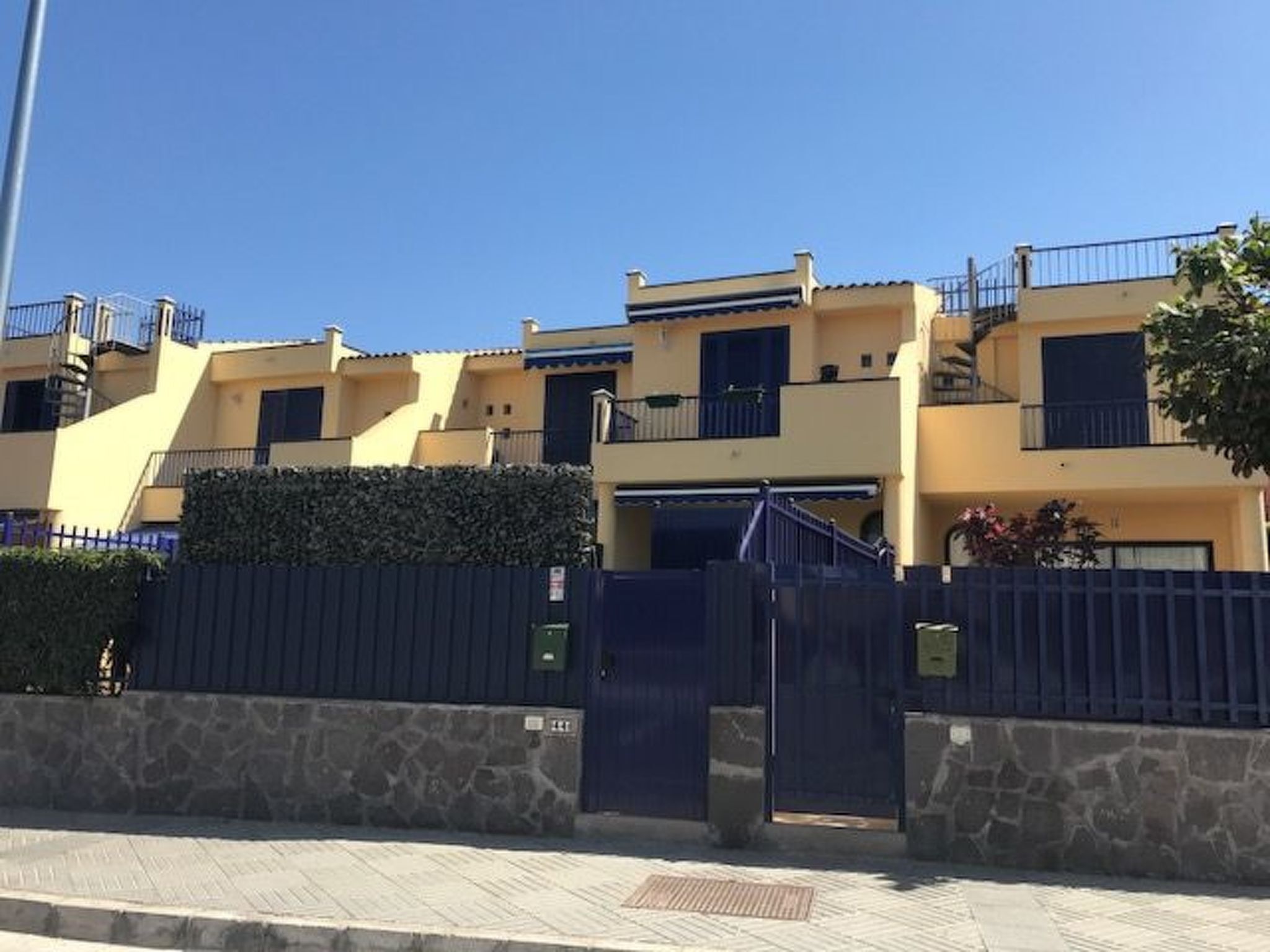 Une rangée de bâtiments jaunes dotés de balcons, un mur de pierre et un portail en métal.