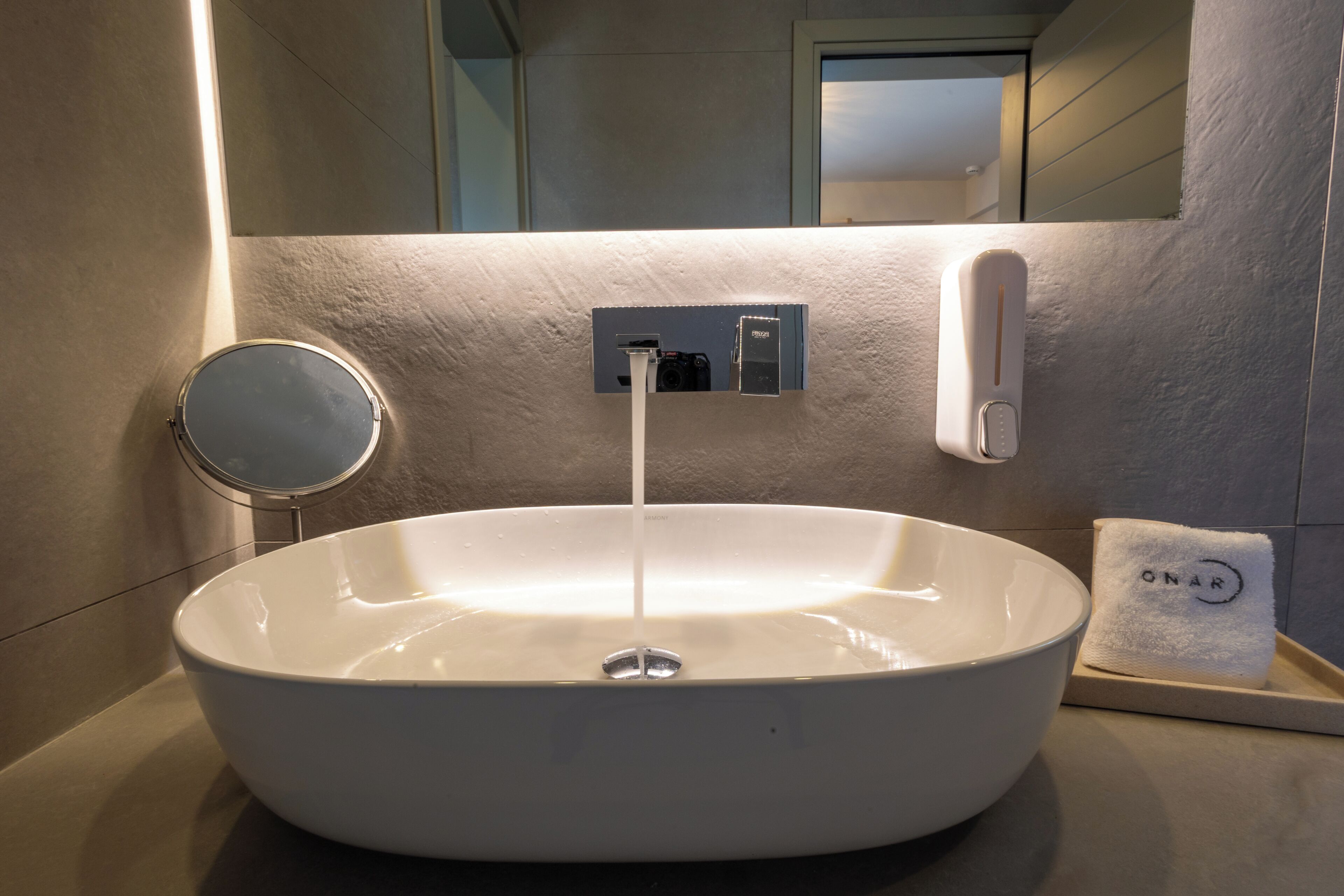 Un lavandino bianco con uno specchio, un dispenser di sapone e un asciugamano su un ripiano.