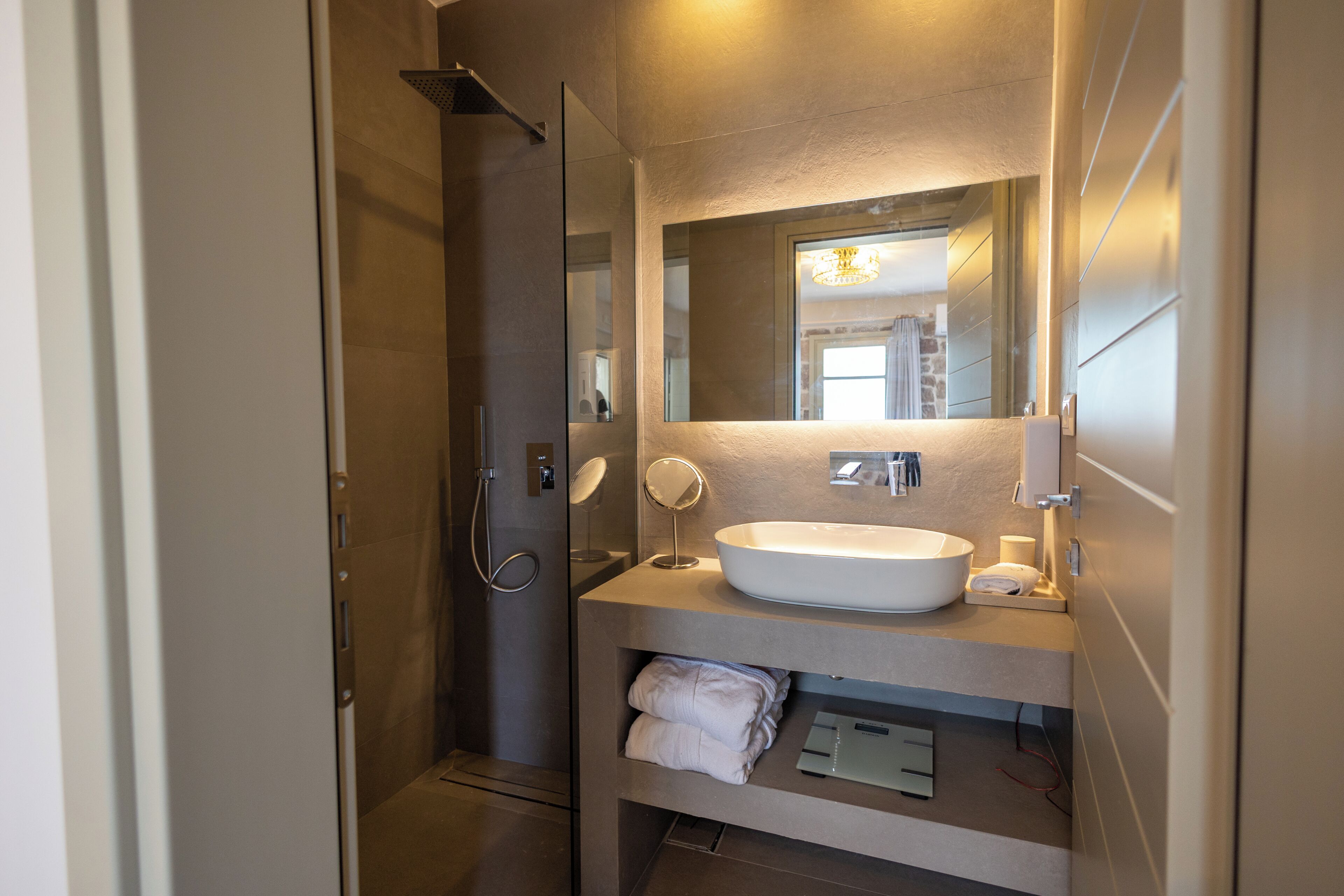 A modern bathroom with a glass-enclosed shower, a large mirror, and a white sink.