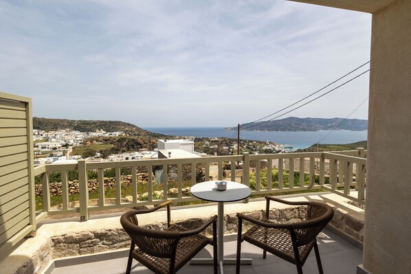 A balcony with wicker chairs and a small table, overlooking a coastal town and sea. - Onar Hotel Kimolos (Kimolos)