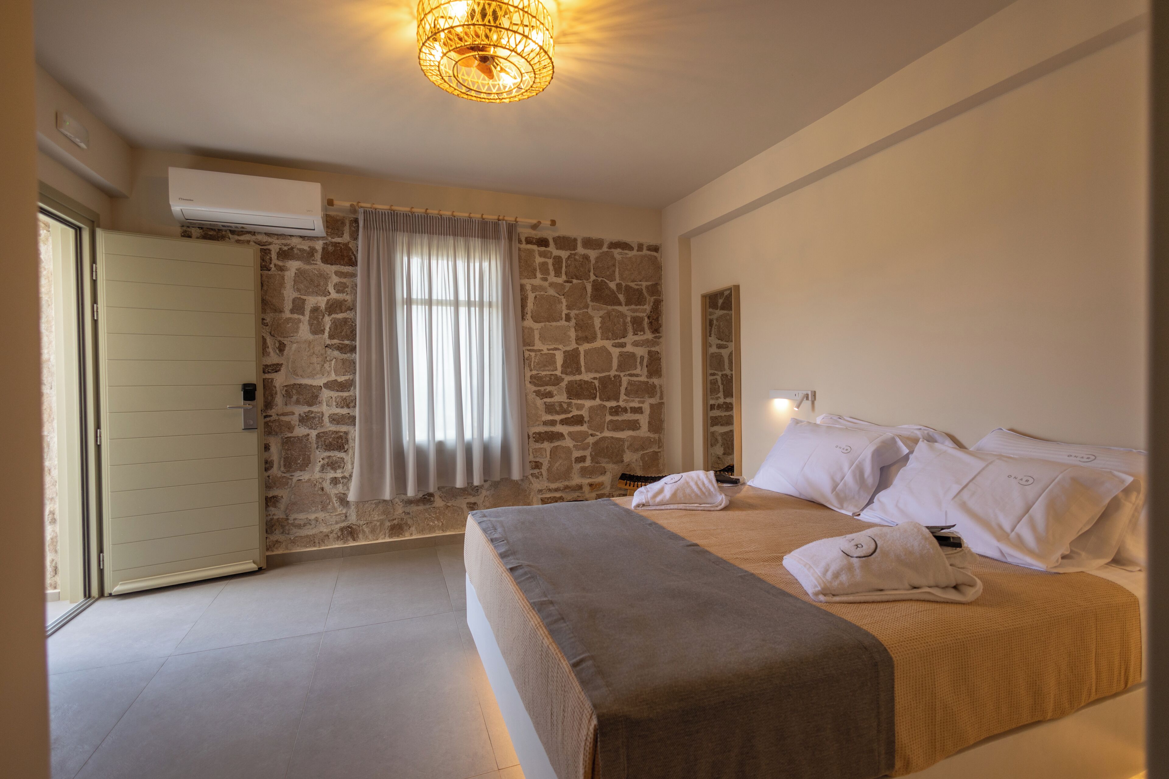A bedroom with a stone wall, a bed with white linens, a bedside table, and a hanging light fixture.