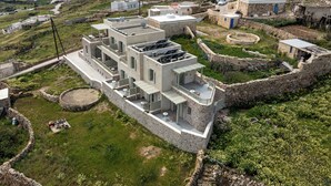 A modern building with multiple balconies, a stone wall surrounding the property, and a view of the sea.