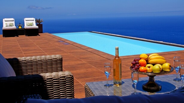 A poolside area with lounge chairs, a table with fruit and drinks, and a view of the ocean. - Moderne Architekten-Villa mit Infinity-Pool und Meerblick by Interhome (Puntagorda)