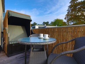 En utomhusplats med sittmöbler i rotting, ett glasbord och stolar, en rutig kudde och ett staket av bambu.