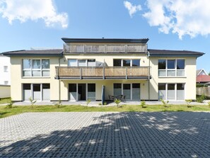 En tvåvånings bostadsbyggnad med en balkong, stora fönster och en asfalterad uppfart.