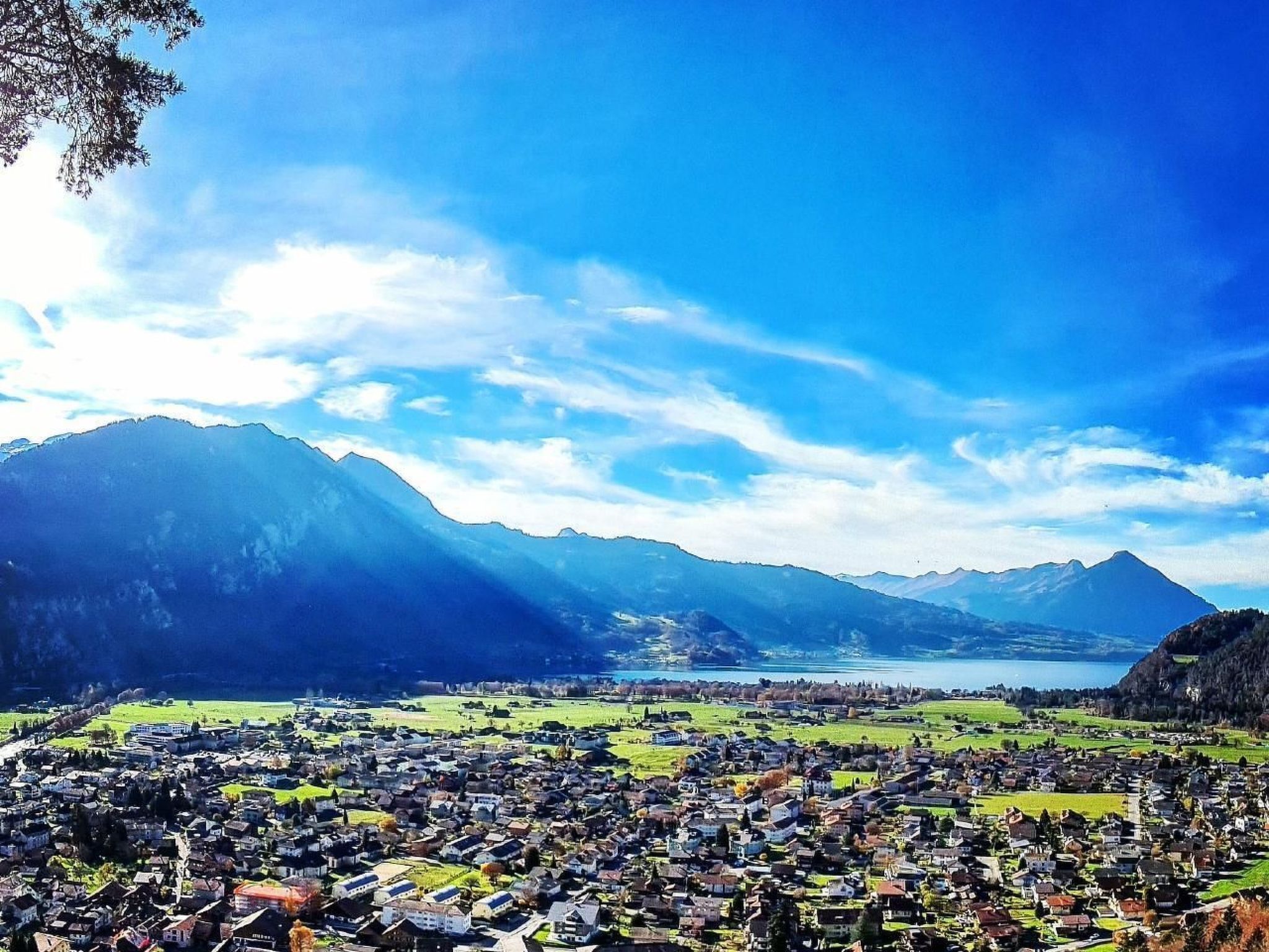 A panoramic view of a town with a lake, mountains, and a clear sky.