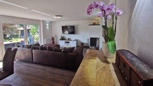 Una sala de estar moderna con un sofá marrón, una mesa de centro de madera y un ventanal grande.