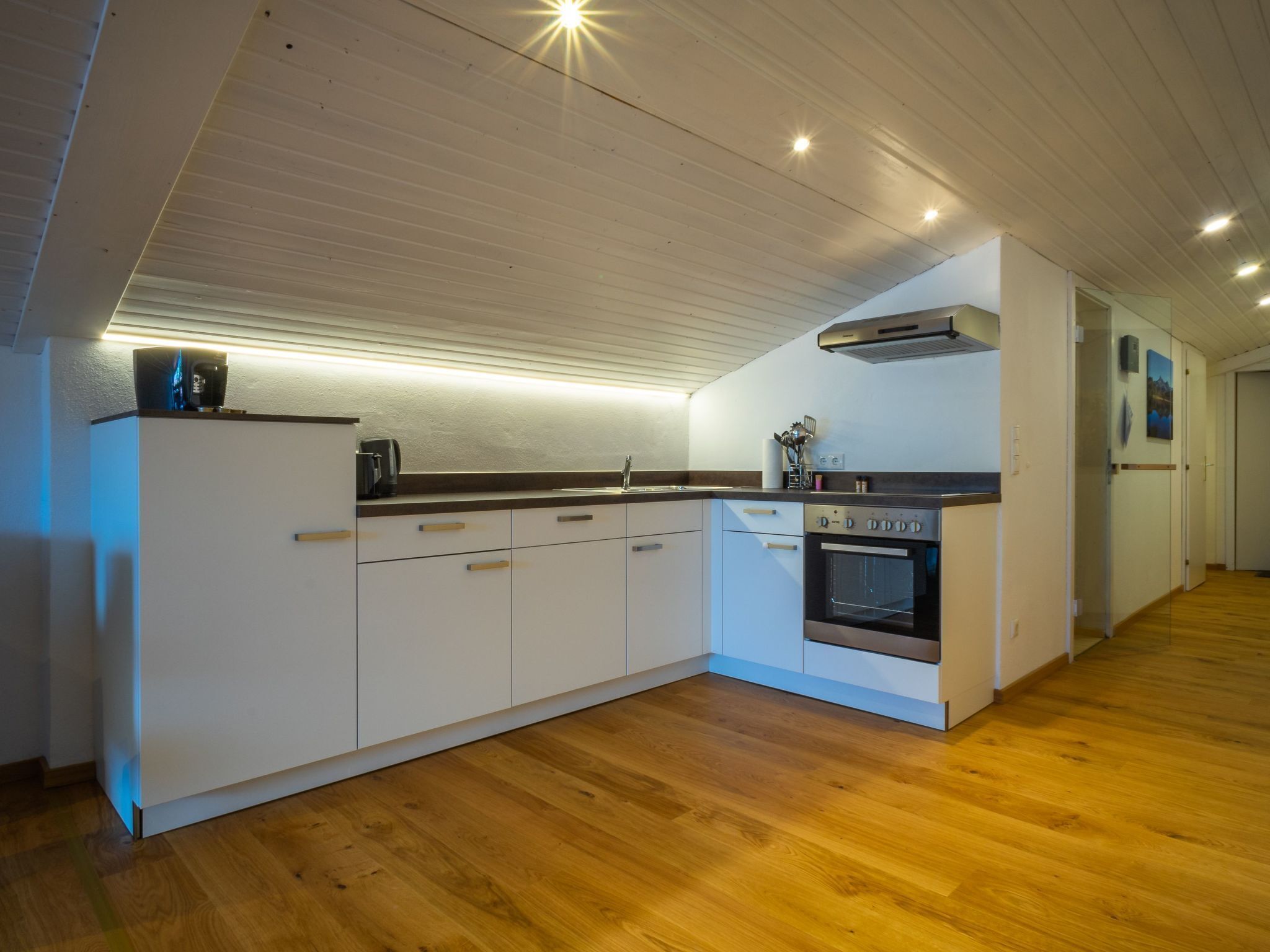 A modern kitchen with white cabinets, a built-in oven, and a wooden floor.