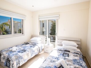 Un dormitorio con dos camas, cada una con una colcha estampada, almohadas blancas y una mesita de noche pequeña.
