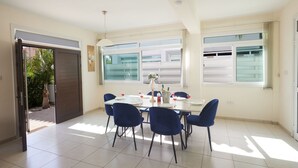 A dining area with a table set for four, blue chairs, and a view of a residential area through large windows. - Hübsche Villa mit 3 Schlafzimmern und privatem Pool by Interhome (Protaras)