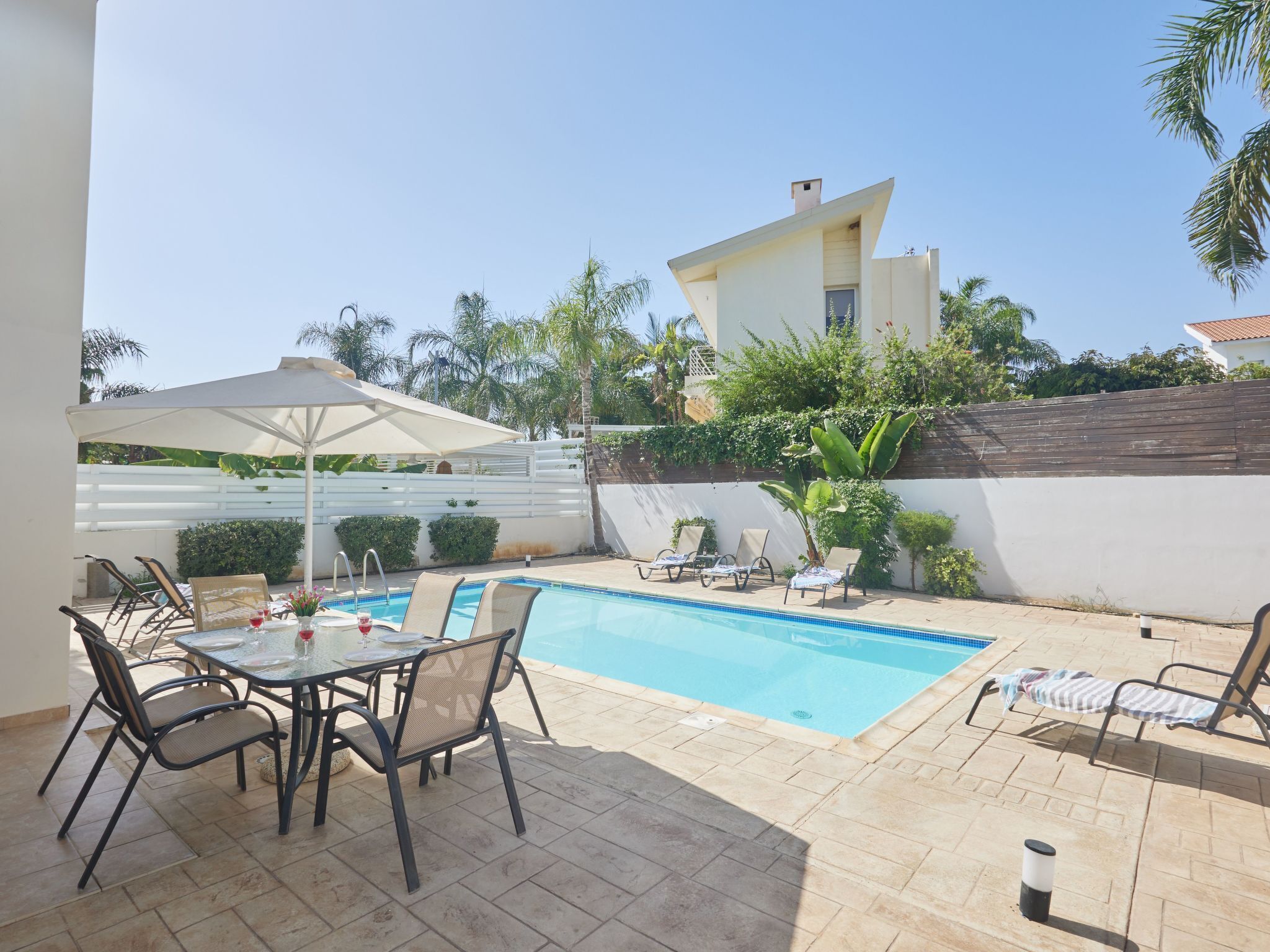 A pool area with lounge chairs, a table with chairs, and a white umbrella.