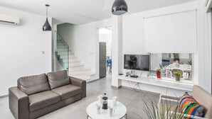 A modern living room with a sofa, coffee table, and a TV. There's a staircase and a dining area visible in the background. - Protaras Greco Villa CCV1 mit beheiztem Pool by Interhome (Paralimni)