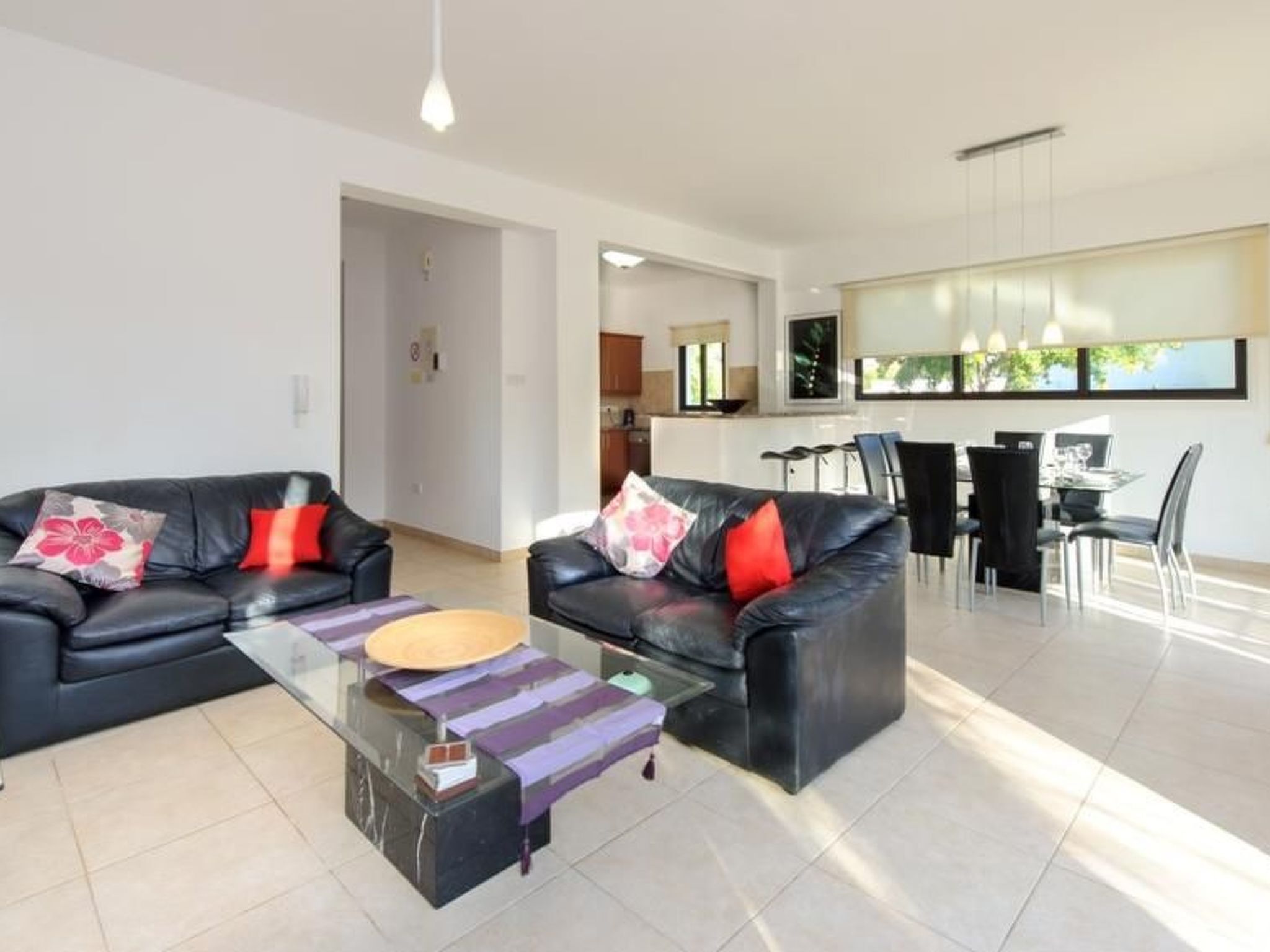 A modern living room with two black leather sofas, a glass coffee table, and a dining area with a black dining table and chairs.