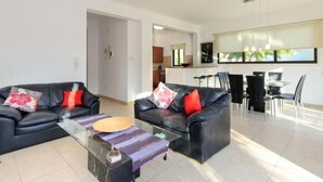 A modern living room with two black leather sofas, a glass coffee table, and a dining area with a black dining table and chairs. - Protaras Ferienvilla AV6 by Interhome (Protaras)