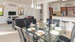 A modern dining area with a glass table set for a meal, surrounded by black chairs. - Protaras Ferienvilla AV6 by Interhome (Protaras)