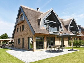 Uma casa moderna com telhado inclinado, grandes janelas e um espaço de varanda com móveis de exterior.