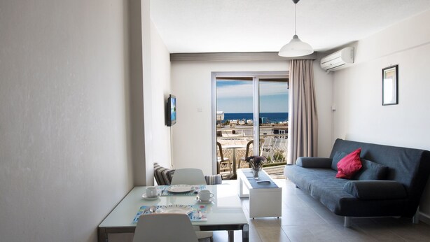 Ein modernes Wohnzimmer mit Essbereich, einem grauen Sofa und einem Balkon mit Meerblick.
