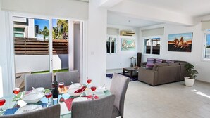 Una sala de estar moderna con un sofá, comedor con una mesa preparada para dos personas y un ventanal con vistas al exterior.