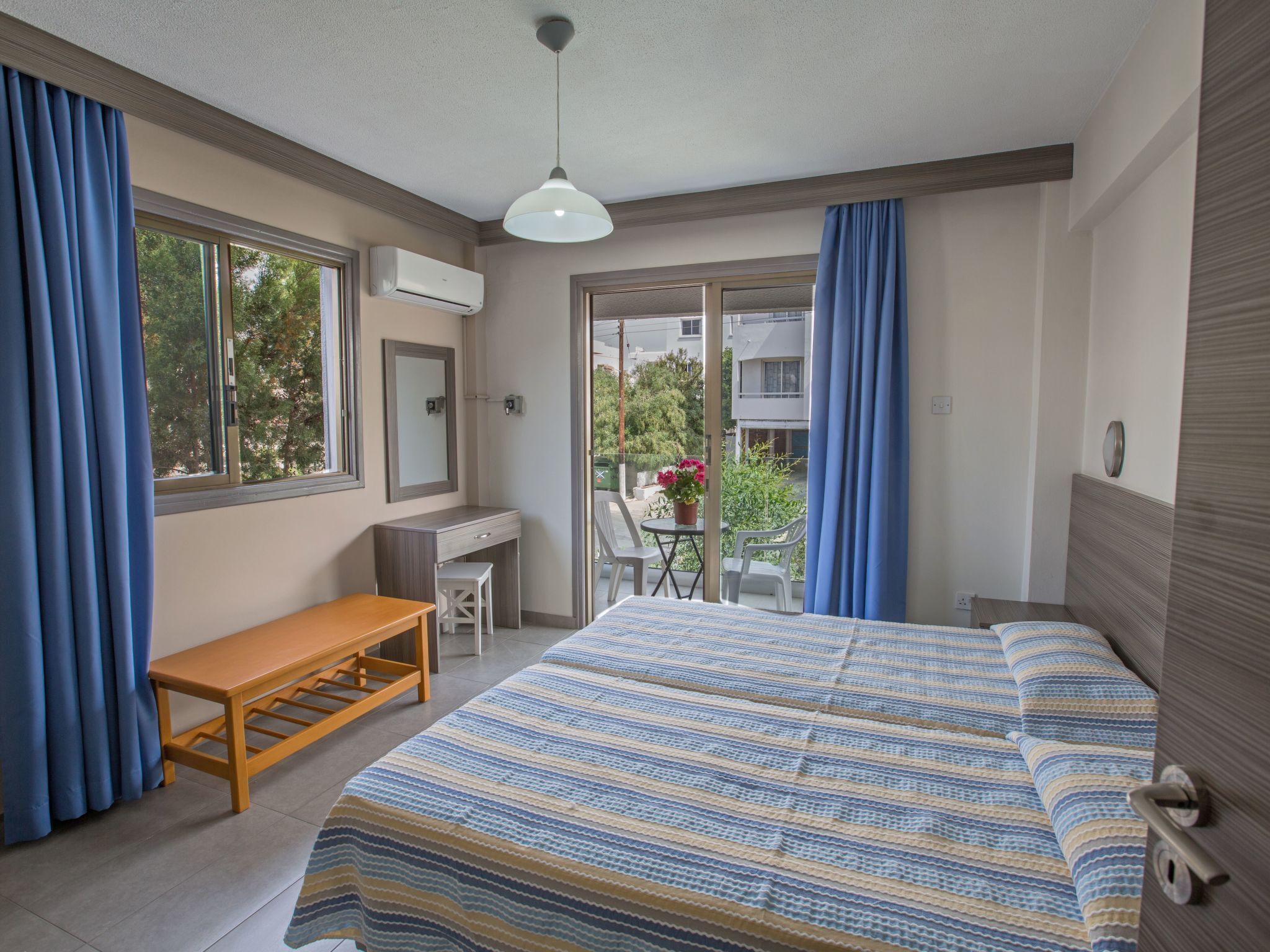 Ein Schlafzimmer mit Bett, Schreibtisch, Stuhl und Blick ins Freie.