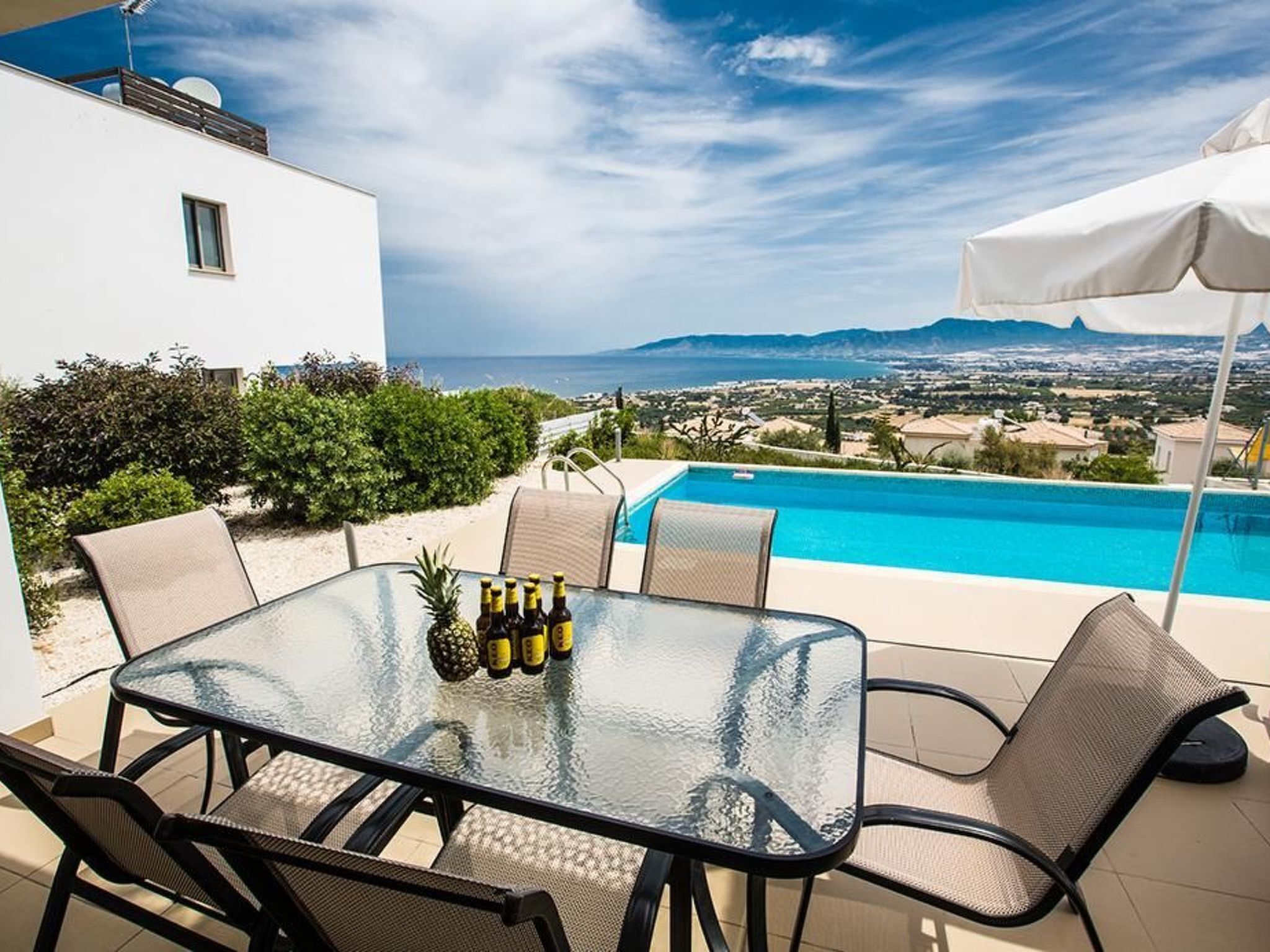 A glass-top table with chairs and a pineapple, overlooking a pool and a scenic view.