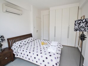 Un dormitorio con cama, mesita de noche, aire acondicionado, armario y lámpara.