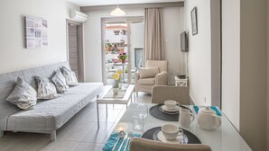 Ein modernes Wohnzimmer mit Sofa, Esstisch und Stühlen. Ein Balkon mit Pflanzen bietet Blick auf die Straße.