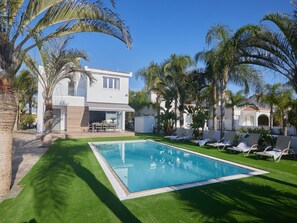 Une maison moderne avec une piscine, entourée de palmiers et d’une pelouse bien entretenue.
