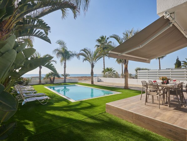Un espace piscine avec vue sur la mer, entouré de palmiers et de chaises longues.