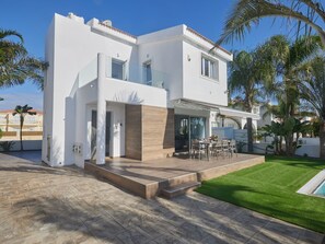 Une maison moderne à deux étages, dotée d’un patio, d’une piscine et d’une végétation luxuriante.