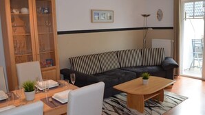 A living room with a striped sofa, a wooden cabinet with glass doors, a dining table with chairs, and a coffee table. - Rügenzauber in Ostseebad Baabe by Interhome (Baabe)