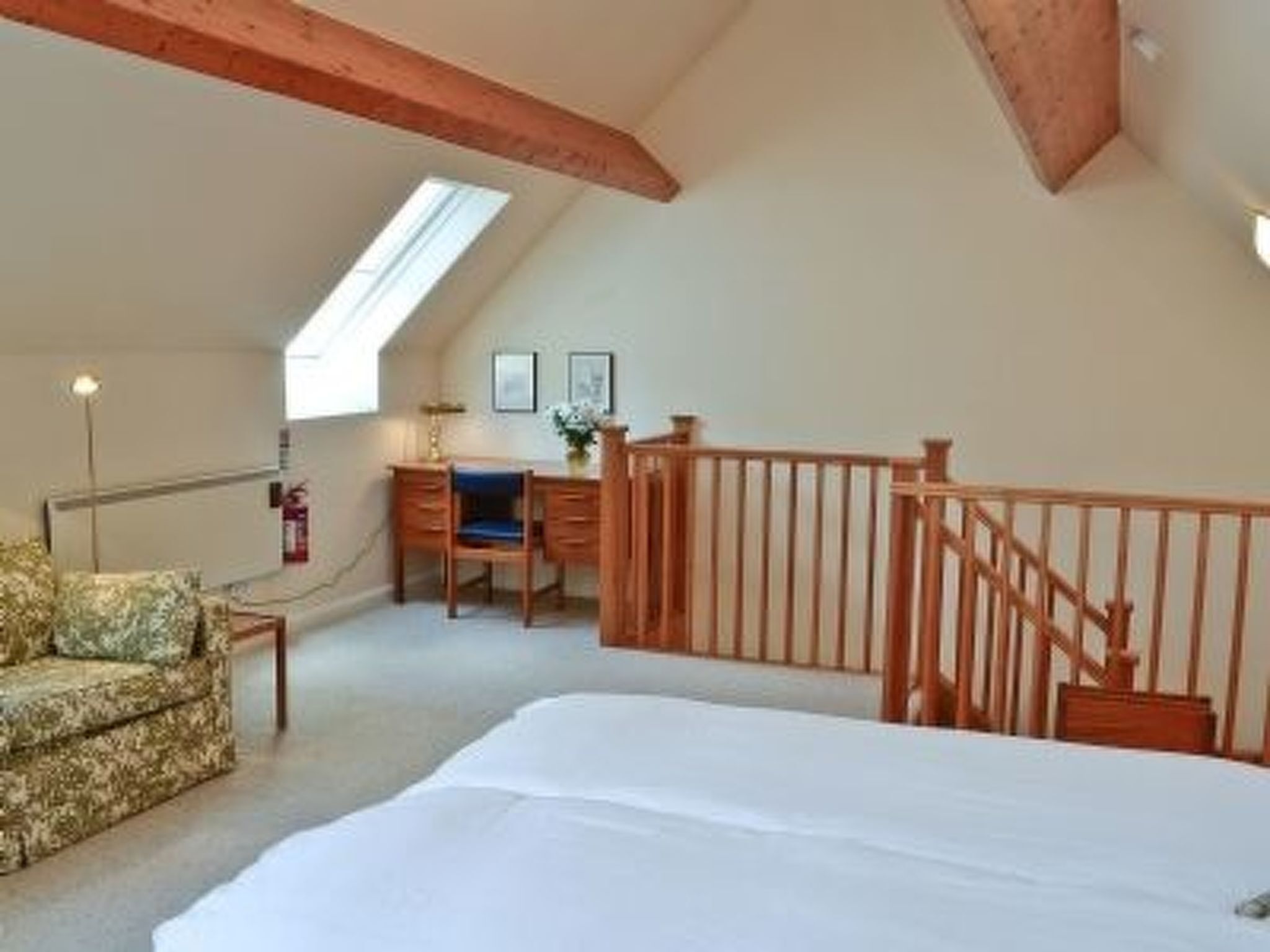 A bedroom with a large bed, a desk with a chair, a small sofa, and a staircase.