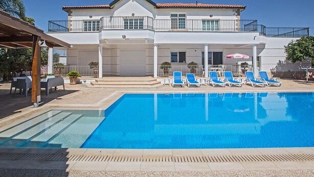 Un edificio de dos pisos con piscina, sillas de descanso y un patio cubierto.