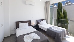 Hotellihuone, jossa on kaksi sänkyä, parveke, jolta on näkymä puistoon, ja seinässä ilmastointilaite.