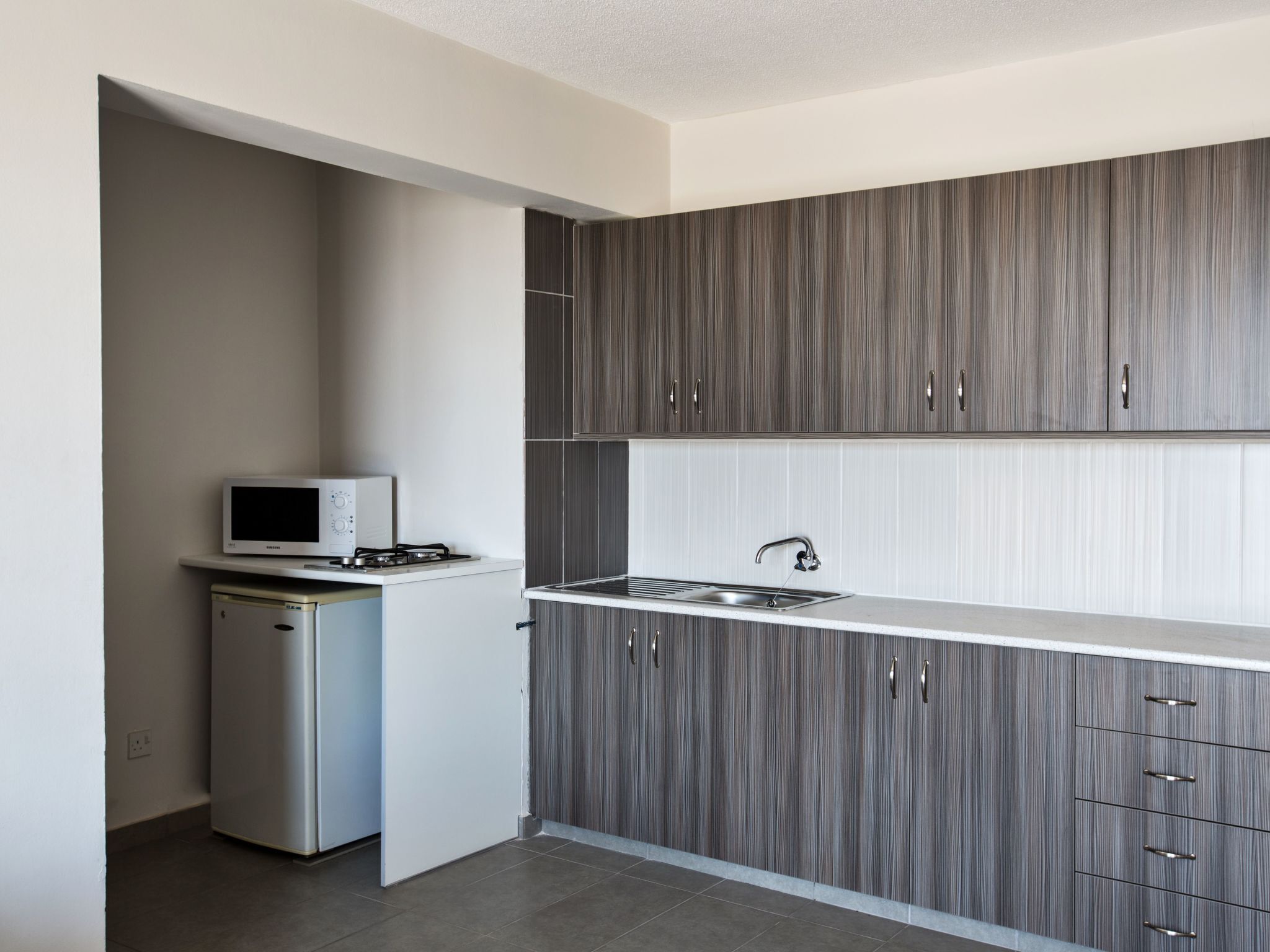 A modern kitchen with grey cabinetry, a built-in microwave, and a stainless steel sink.
