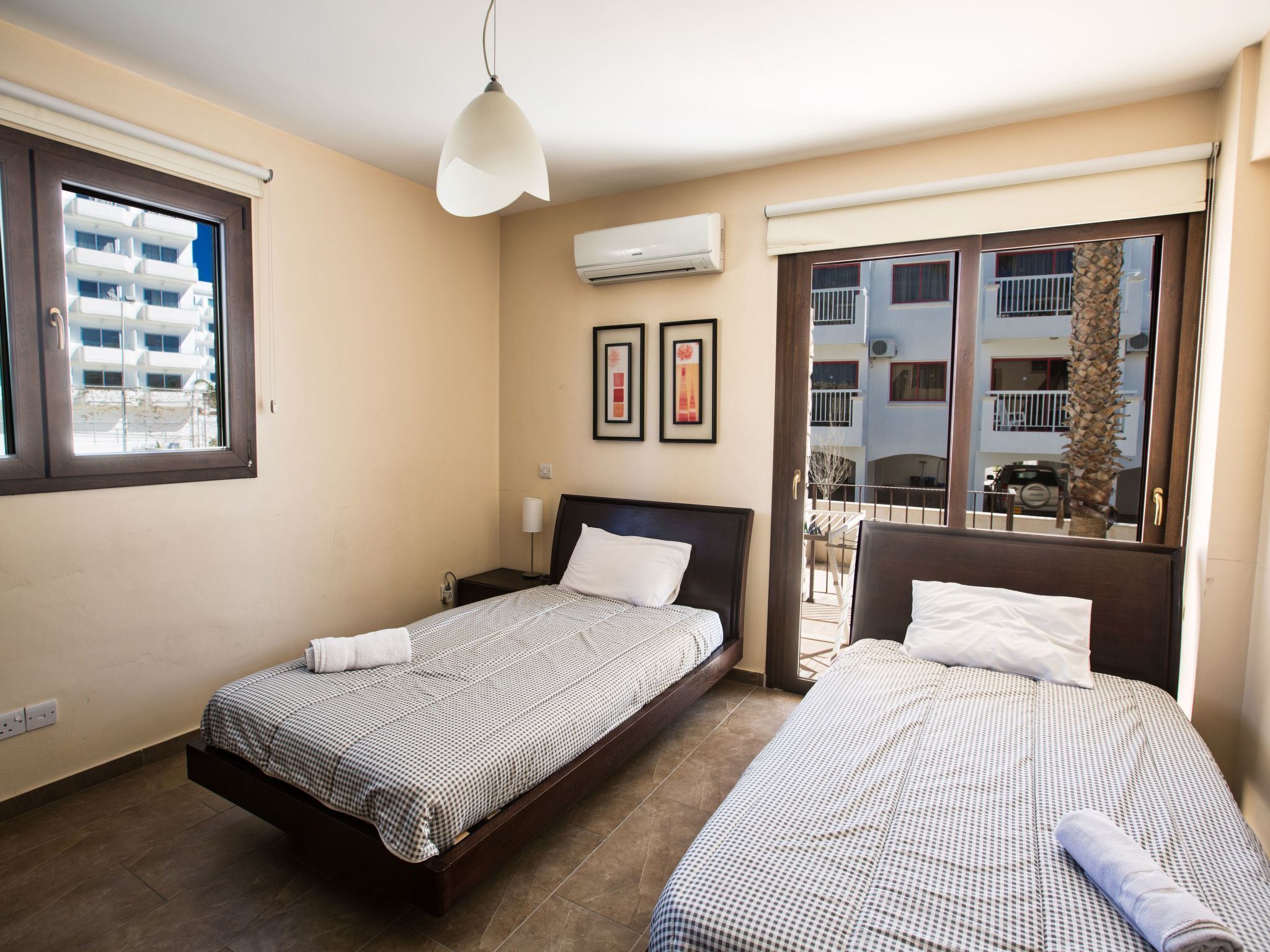 Een hotelkamer met twee bedden, een plafondlamp, een airconditioner en uitzicht op het balkon.