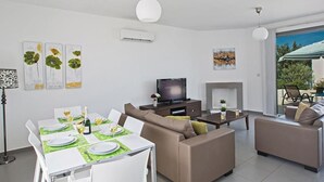 A modern living room with a dining area, a flat-screen TV, and a fireplace. - Latchi Ferienvilla EV26 by Interhome (Agios Georgios Pegeias)