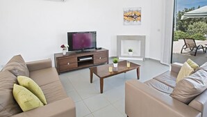 A modern living room with a flat-screen TV, a fireplace, and a view of the outdoors. - Latchi Ferienvilla EV26 by Interhome (Agios Georgios Pegeias)
