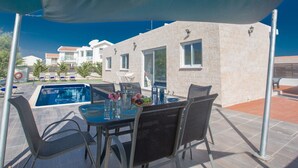 Area piscina con tavolo apparecchiato per mangiare, sedie da esterno e ombrellone.