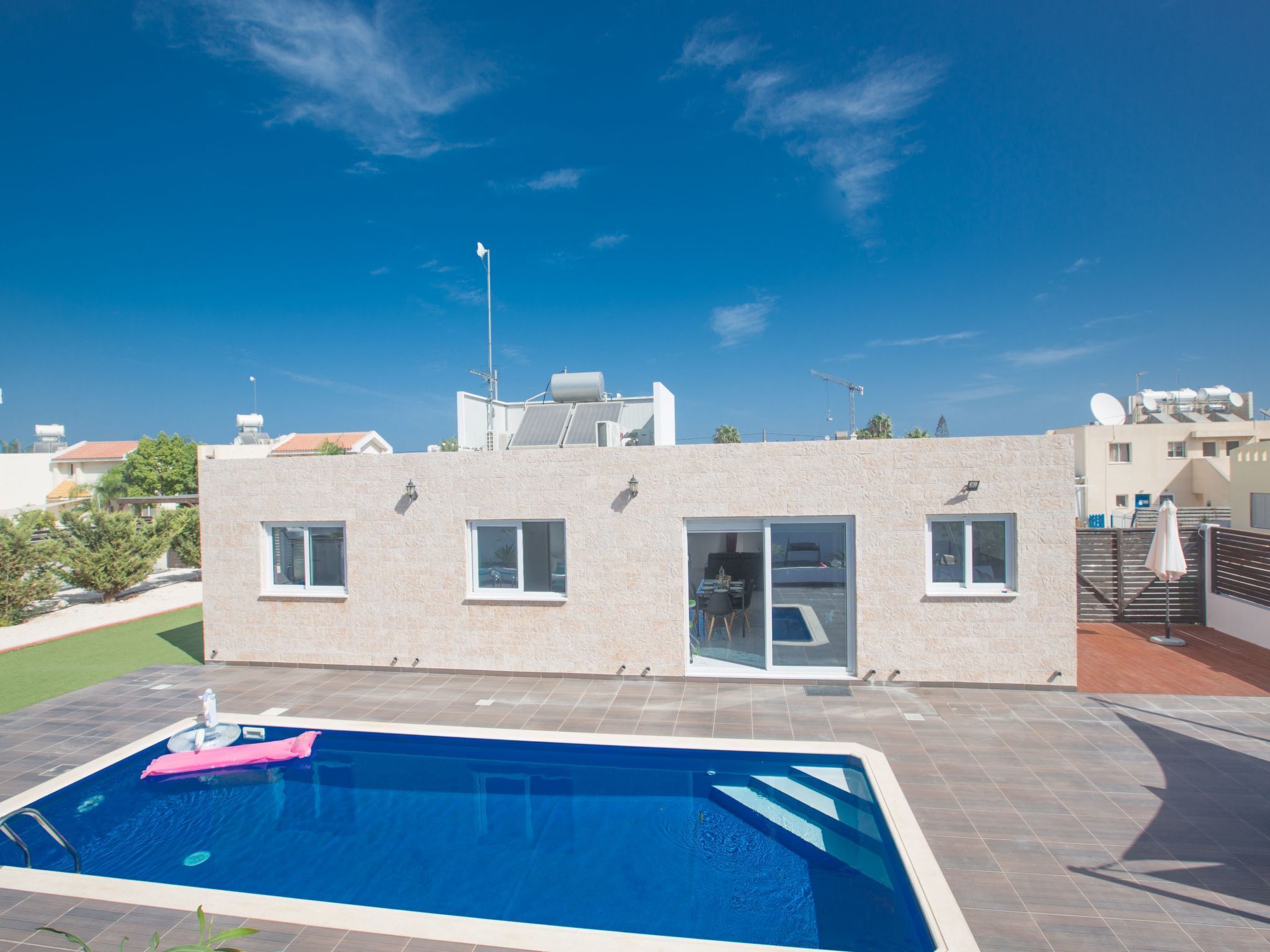 A modern building with a swimming pool, large windows, and a flat roof with solar panels.