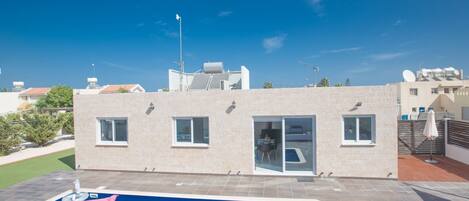A modern building with a swimming pool, large windows, and a flat roof with solar panels.