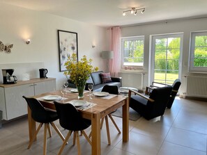 A modern dining area with a wooden table set for four, surrounded by black chairs. There is a vase with yellow flowers on the table, and a coffee machine on the counter to the left. - Moderne 2-Zimmer Ferienwohnung by Interhome (Baabe)